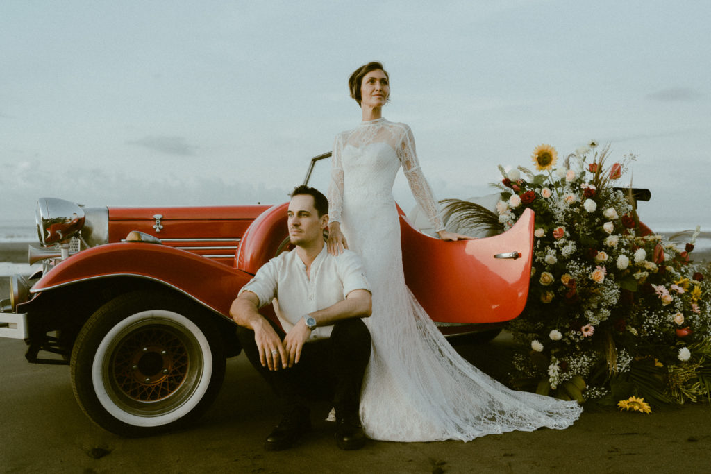 bride and groom standing next to a vintage car on the beach at their Bali elopement