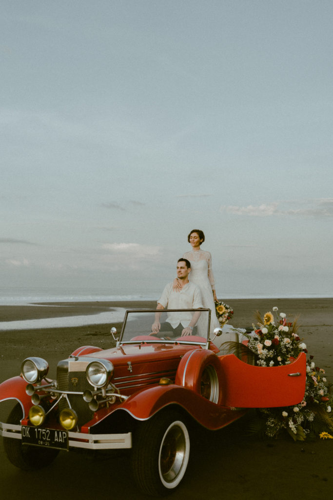 bride and groom standing on vintage convertible on beach at their bali elopement