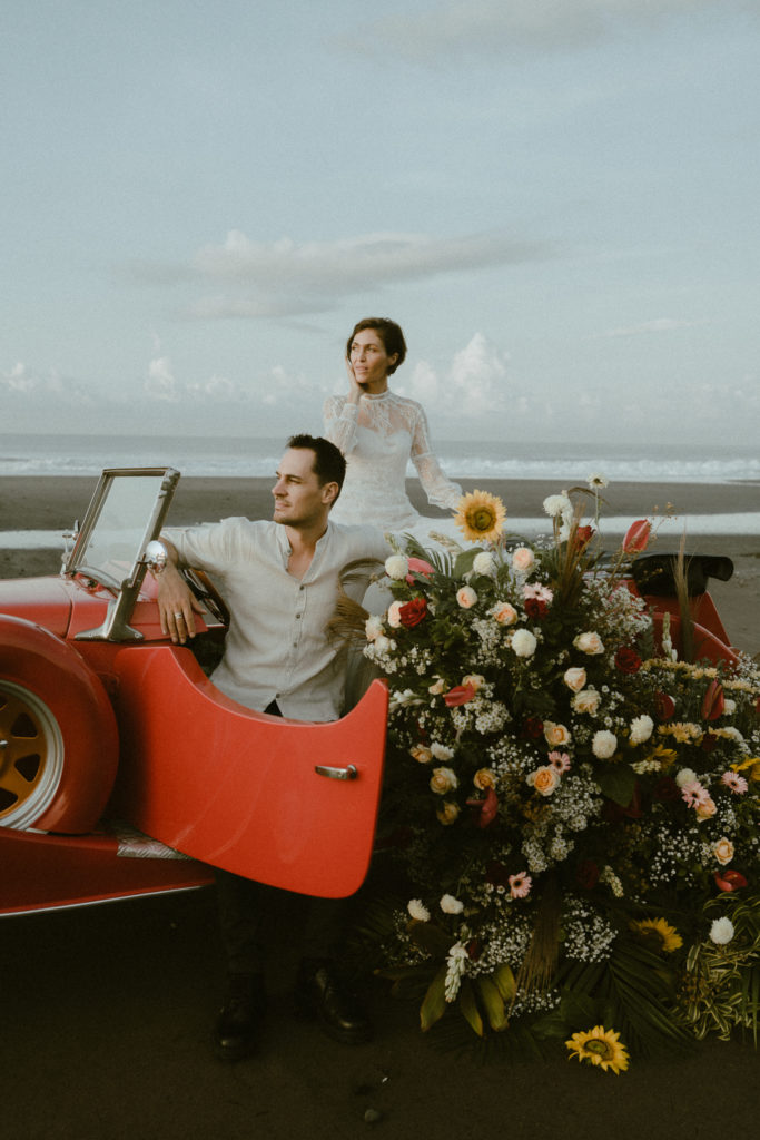 bride and groom sitting on vintage convertible on beach at their bali elopement