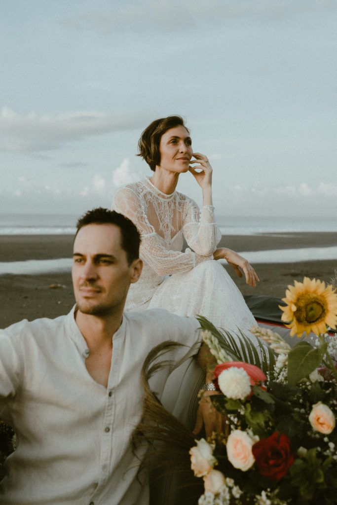 groom and bride sitting together on vintage convertible covered in flowers while they look off into the distance at their bali elopement