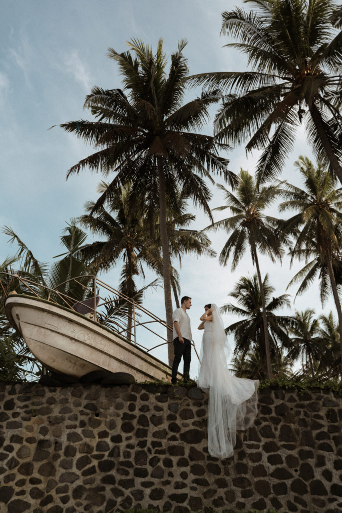 bride and groom standing near a shipwrecked boat at their bali elopement