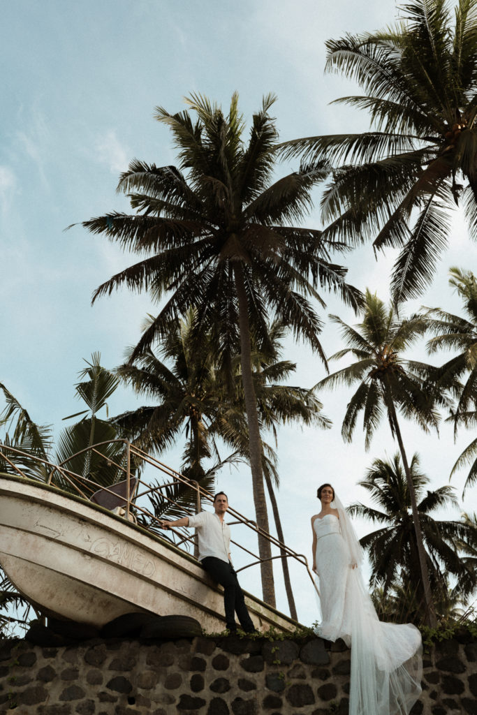 bride and groom standing near a boat at their bali elopement