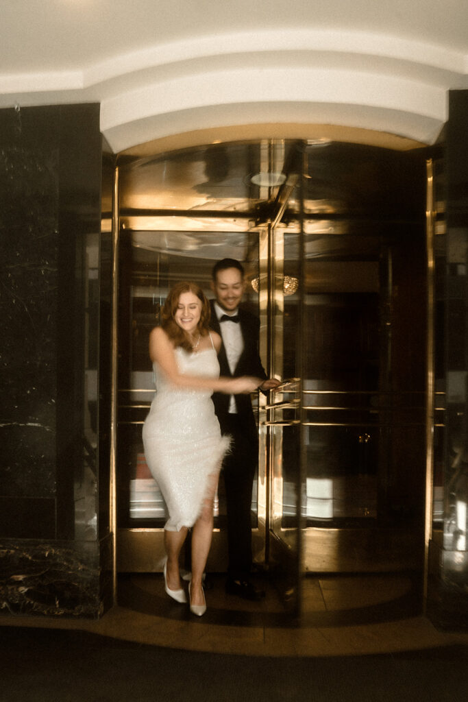 Couple sharing a playful moment in The Benson Hotel's revolving door during their Portland engagement photo session.