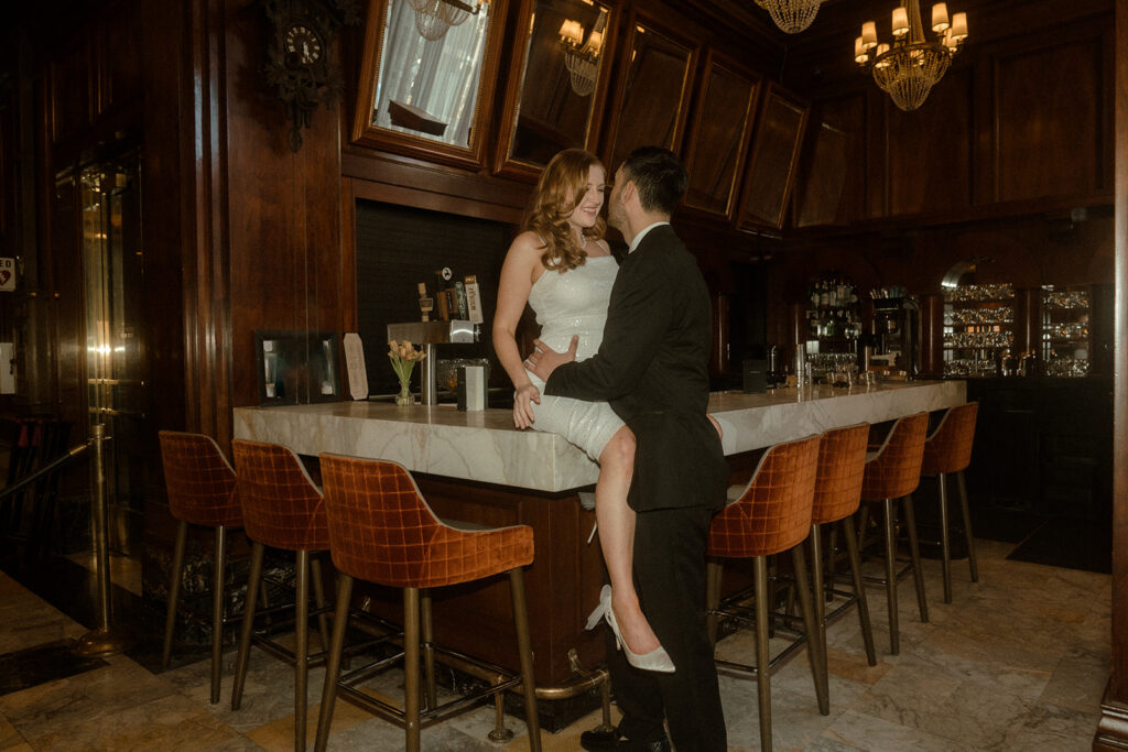 Portland engagement photos showcase a couple's playful exchange beside The Benson Hotel's elegant bar.
